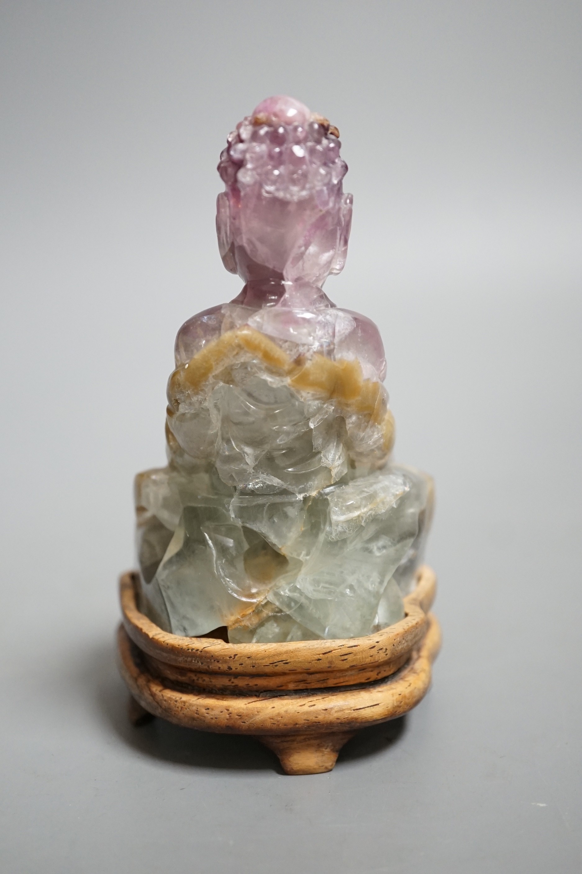 A 19th century amethyst and green quartz carving of a seated buddha on hardwood stand. Height 12cm